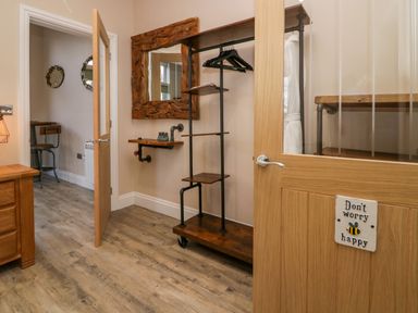 An entryway with a wooden shelving unit with hangers a wall-mounted wooden shelf a large wooden framed mirror and a door with a sign that says dont worry be happy at Elderflower Lodge in Allithwaite near Cartmel