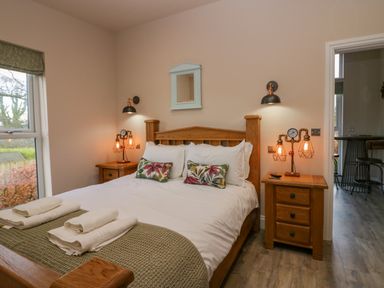 A bedroom with a wooden bed frame two bedside tables with lamps and folded towels at Elderflower Lodge in Allithwaite near Cartmel