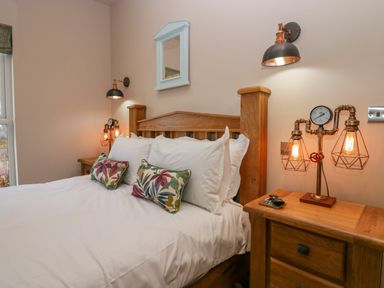 A bedroom with a wooden bed and bedside tables with industrial lamps at Elderflower Lodge in Allithwaite near Cartmel