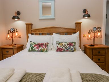 A bedroom with a wooden bed frame two bedside tables lamps and a mirror at Elderflower Lodge in Allithwaite near Cartmel