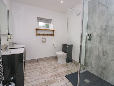 A bathroom with a double sink vanity a toilet a glass shower enclosure and a wooden shelf on the wall at Elderflower Lodge Allithwaite near Cartmel