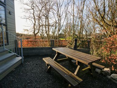 An outdoor area with a wooden picnic table and benches next to a building and leafless trees at Elderflower Lodge in Allithwaite near Cartmel