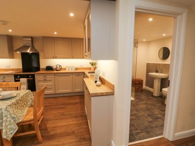 A kitchen with dining table and chairs next to a bathroom with sink toilet and mirror at 1 Brookside Warcop