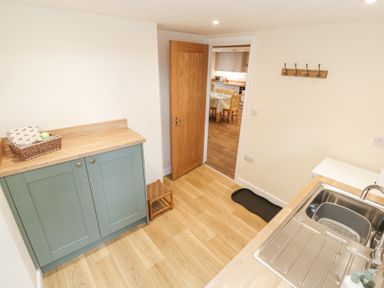 A utility room with green cabinets a wooden countertop a stainless steel sink and an open door leading to a kitchen at 1 Brookside in Warcop