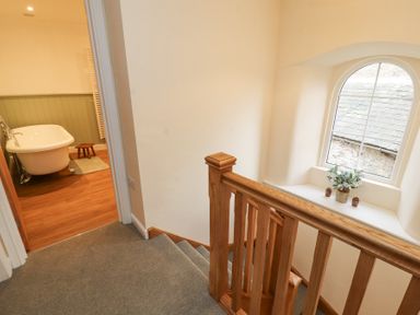 A staircase with wooden handrails next to a bathroom with a freestanding bathtub and wooden floor at 1 Brookside in Warcop
