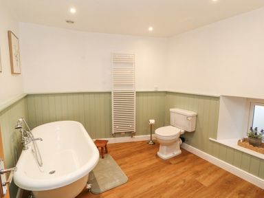 A bathroom with a bathtub a toilet a towel radiator and a window with a plant at 1 Brookside in Warcop