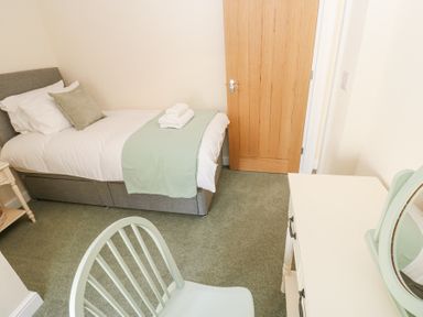 A bedroom with a single bed a wooden door a white desk with a mirror and a chair at 1 Brookside in Warcop