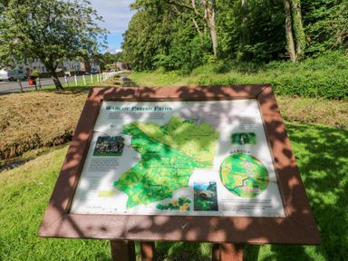 An outdoor information board displaying a map of Warcop Parish Paths beside a road and trees at 1 Brookside in Warcop