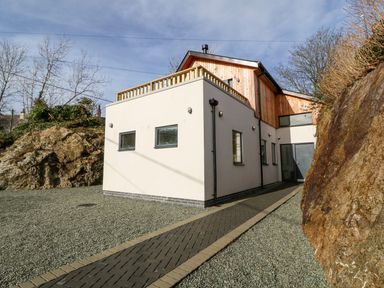 A modern two story house with a pathway and gravel ground between rocks at Ty Chwarel in Menai Bridge