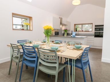 A dining table set with plates bowls glasses and cutlery surrounded by chairs in an open kitchen and dining area at Ty Chwarel in Menai Bridge