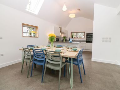 A dining area with a table set with plates and bowls and blue and gray chairs in a kitchen at Ty Chwarel in Menai Bridge