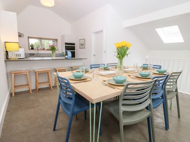 A dining area with a table set for eight and an open kitchen with stools at Ty Chwarel in Menai Bridge