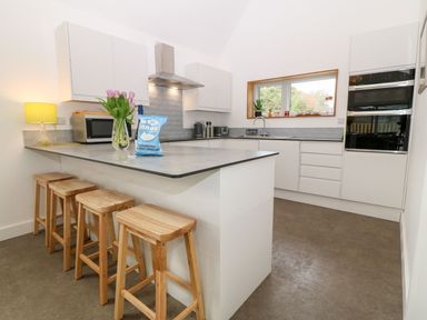 A white kitchen with a countertop island and wooden stools at Ty Chwarel in Menai Bridge
