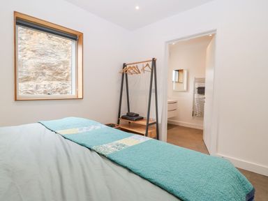 A bedroom with a bed covered in a blue quilt next to a window and an open door leading to a bathroom at Ty Chwarel in Menai Bridge