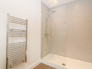 A bathroom with a walk-in shower with glass partition and a wall-mounted towel radiator at Ty Chwarel in Menai Bridge