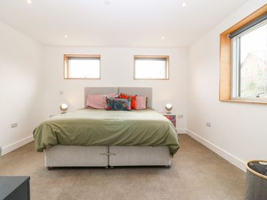 A bedroom with a double bed green bedspread two rectangular windows above the bed and a window on the right at Ty Chwarel in Menai Bridge