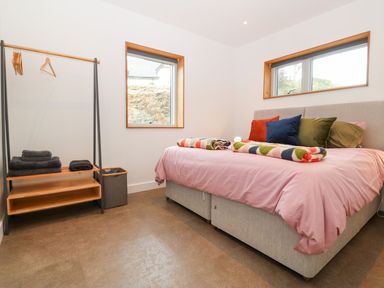 A bedroom with a bed with colorful pillows and folded blankets and a clothes rack with hangers and towels at Ty Chwarel in Menai Bridge