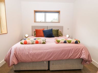 A bedroom with a double bed with colorful pillows and blankets under a window at Ty Chwarel in Menai Bridge