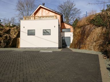 A modern house with a paved driveway and rocky walls on both sides at Ty Chwarel in Menai Bridge