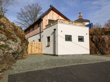 A modern two-story house with wooden siding and white walls surrounded by rock formations at Ty Chwarel in Menai Bridge