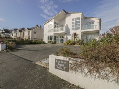 A two-story white house with balconies and large windows with a driveway and garden at Seaview in Benllech near Red Wharf Bay