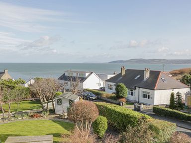 A garden with green bushes and a wooden shed near houses by the sea at Seaview in Benllech near Red Wharf Bay