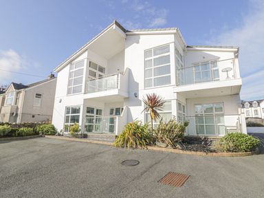 A two story white residential building with balconies and large windows in a suburban area at Seaview in Benllech near Red Wharf Bay