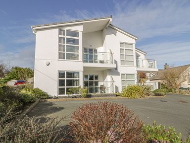 A modern two-story white house with balconies and large windows surrounded by shrubs and a driveway at Seaview in Benllech near Red Wharf Bay