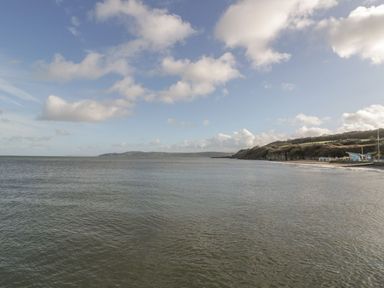 A coastal view with water beach and hills under a partly cloudy sky at Seaview in Benllech near Red Wharf Bay