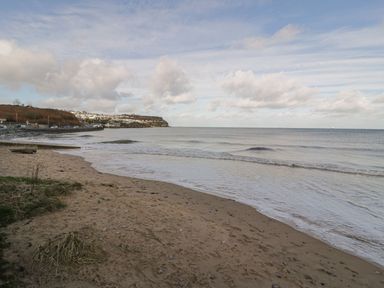 A sandy beach with small waves and houses on a hillside in the background at Seaview in Benllech near Red Wharf Bay