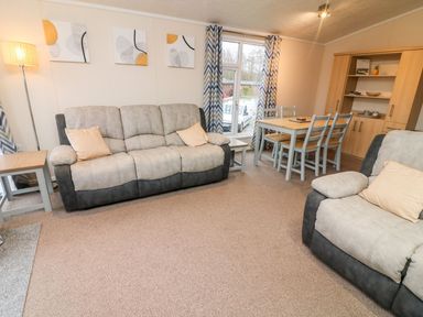 A living room with sofas a dining table chairs a floor lamp and a wooden cabinet at 6 Sherwood in Carnforth near Tewitfield