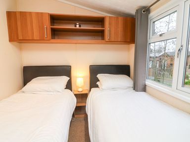 A bedroom with two single beds with white bedding and a small lamp on a nightstand between the beds at 6 Sherwood in Carnforth near Tewitfield