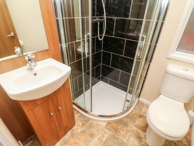 A bathroom with a white sink on a wooden cabinet a glass shower with black tiles and a white toilet at 6 Sherwood Carnforth near Tewitfield