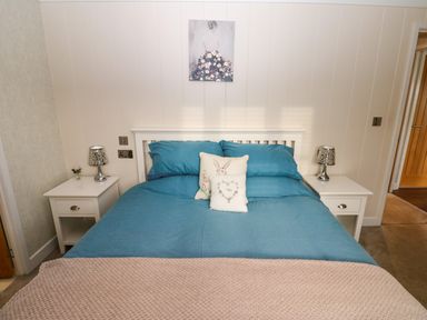 A bedroom with a blue bedspread two white bedside tables with lamps and a painting above the bed at Finnbars Lodge in Richmond