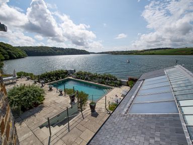 A patio with a swimming pool overlooking a river with green hills and a boat in the distance at Curlew House in Cosheston