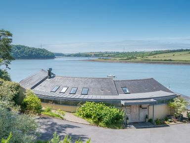 A curved roof house by a river with green hills in the background at Curlew House in Cosheston