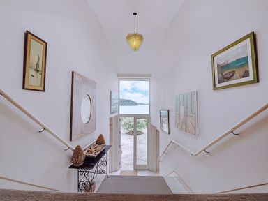 A stairway with handrails leading down to glass doors showing an outdoor view with water at Curlew House in Cosheston