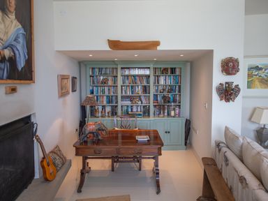 A study room with a wooden desk, a chair, bookshelves, a guitar, and decorative items at Curlew House in Cosheston