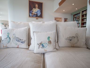 A beige sofa with duck printed cushions and a portrait painting on the wall at Curlew House in Cosheston
