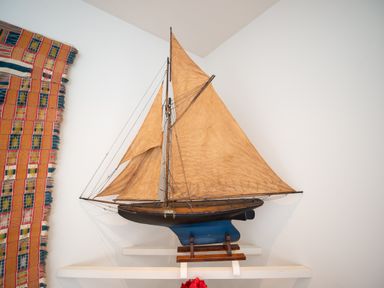 A model sailboat with tan sails on a white shelf next to a colorful woven textile on a white wall at Curlew House in Cosheston