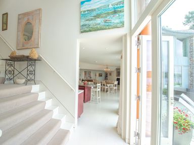 A stairway with carpet and a decorative table beside it leading to an open dining area with chairs and a chandelier at Curlew House in Cosheston