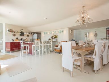 A kitchen with white bar stools and a dining room with a wooden table and white covered chairs at Curlew House in Cosheston