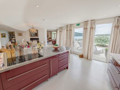 A kitchen with a red island and utensils near a dining area and glass doors opening to a patio at Curlew House in Cosheston