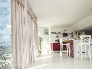 A kitchen with white chairs red cabinets and a large window with closed curtains at Curlew House in Cosheston