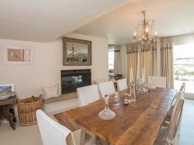 A dining room with a wooden table and white covered chairs a chandelier and a fireplace at Curlew House in Cosheston