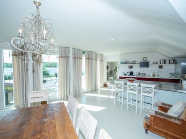 A dining table with chairs and a chandelier next to a kitchen with a counter and bar stools at Curlew House in Cosheston