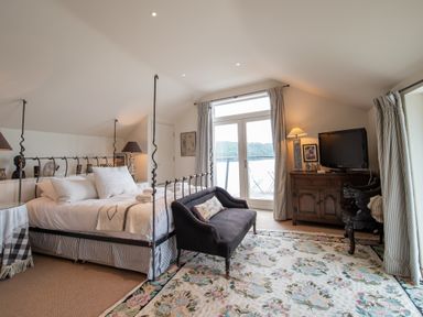 A bedroom with a four-poster bed a small sofa a wooden cabinet with a television and patio doors with curtains at Curlew House in Cosheston