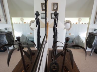 A room with a sink a bathtub a lamp and decorative items reflected in a mirror at Curlew House in Cosheston