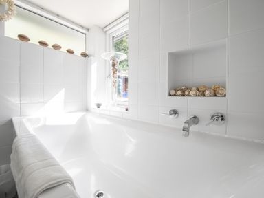 A white bathtub with a towel on the edge and decorative shells in a niche and on a windowsill in a bathroom at Curlew House in Cosheston
