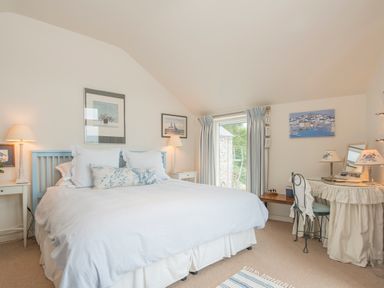 A bedroom with a double bed nightstands lamps a dressing table and a window with curtains at Curlew House in Cosheston